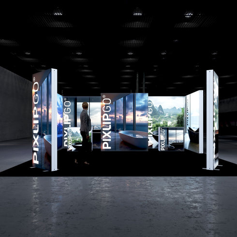 Front view of an illuminated PIXLIP GO exhibition booth showcasing vibrant panoramic cityscapes and natural landscapes, integrated with high-end bathroom interiors. The setup includes a black floor that enhances the visuals.